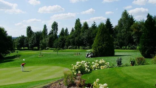 Golfplatz mit Golfer, Bollerwagen und blühendem Garten bei sonnigem Wetter