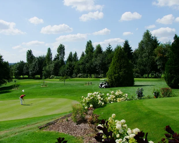 Golfplatz mit Golfer, Bollerwagen und blühendem Garten bei sonnigem Wetter