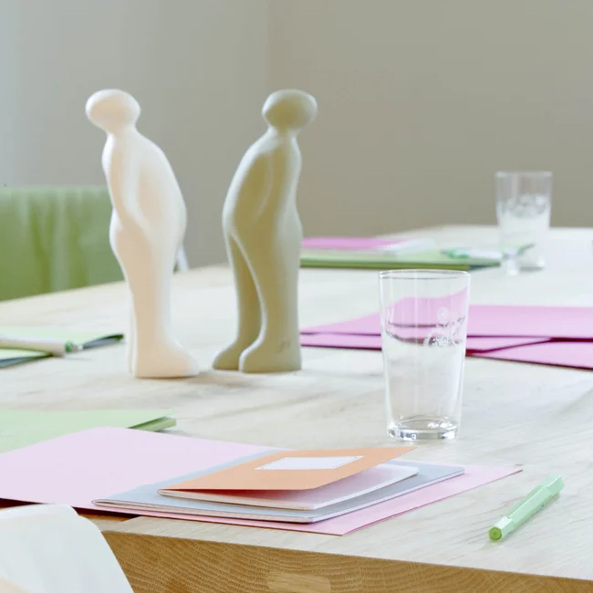 Konferenztisch mit Papier, Stiften, Glas Wasser und zwei abstrakten Figuren