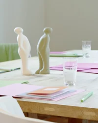 Konferenztisch mit Papier, Stiften, Glas Wasser und zwei abstrakten Figuren