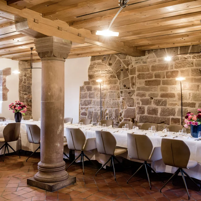 Historischer Bankettsaal mit Holzdecke, Steinsäule und gedecktem Tisch