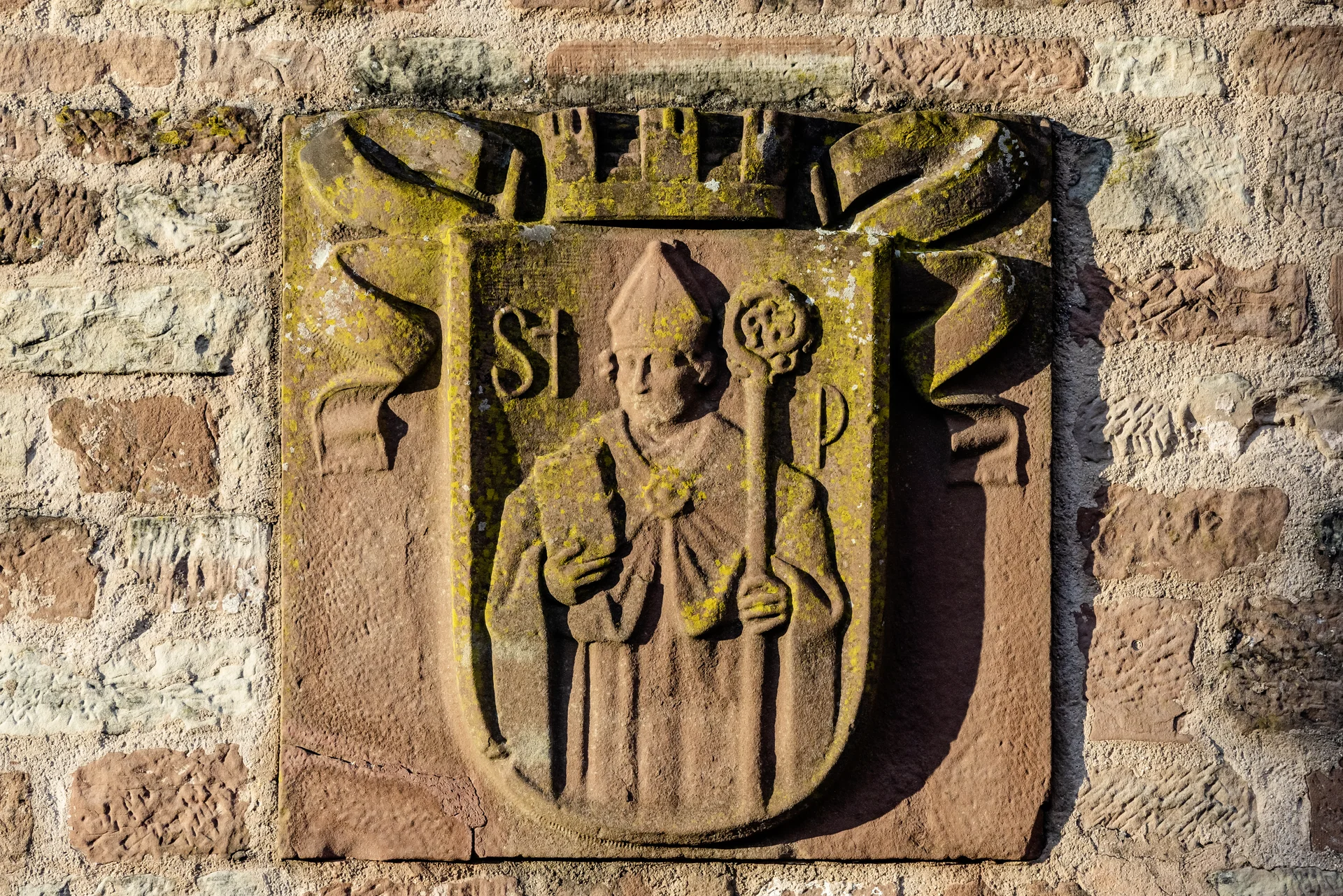 Steinrelief eines Bischofs mit Mitra und Stab an einer Steinmauer