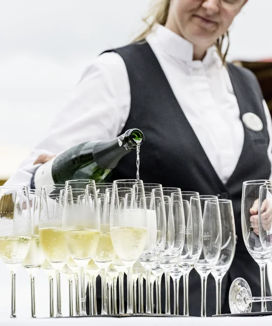 Kellnerin gießt Sekt in mehrere Reihen von Gläsern