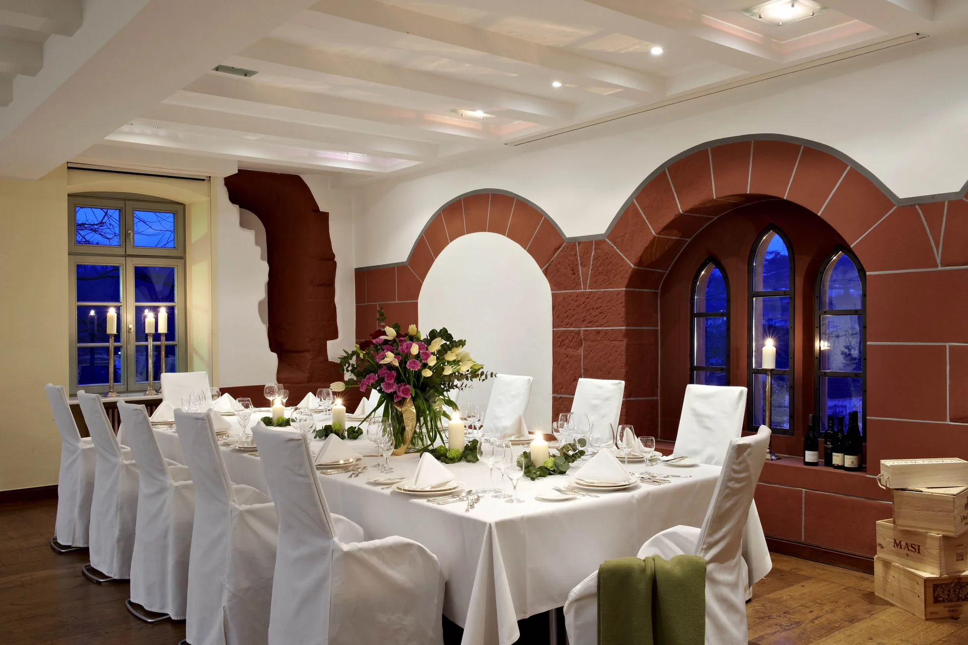 Eleganter Essbereich mit weiß gedecktem Tisch und Kerzenlicht neben Bogenfenstern