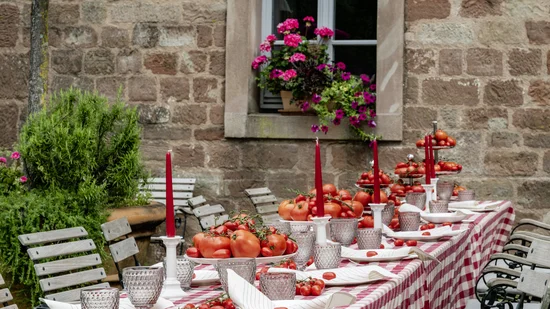 Langer Tisch im Freien mit kariertem Tuch, roten Kerzen und vielen Tomaten