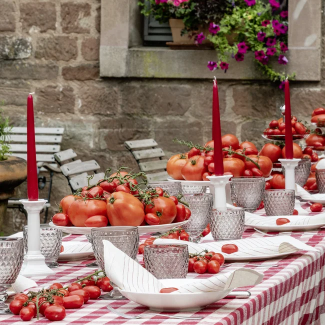 Langer Tisch im Freien mit kariertem Tuch, roten Kerzen und vielen Tomaten