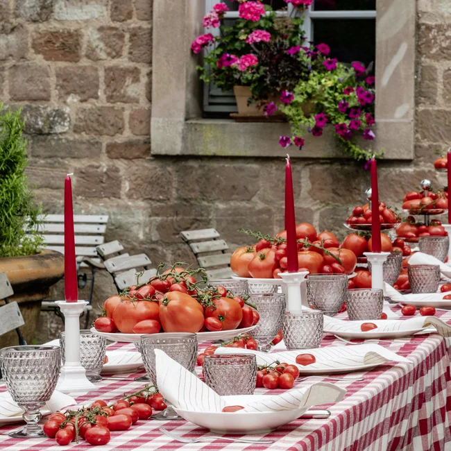 Langer Tisch im Freien mit kariertem Tuch, roten Kerzen und vielen Tomaten
