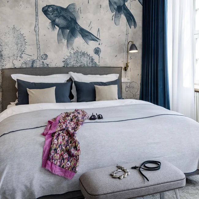 Schlafzimmer mit Wandbild von Fischen, graues Bett und pinke Tasche am Fenster