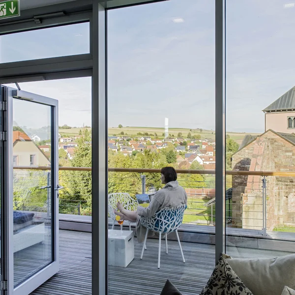 Person sitzt mit Laptop auf Balkon mit Blick auf Dorf und Kirche