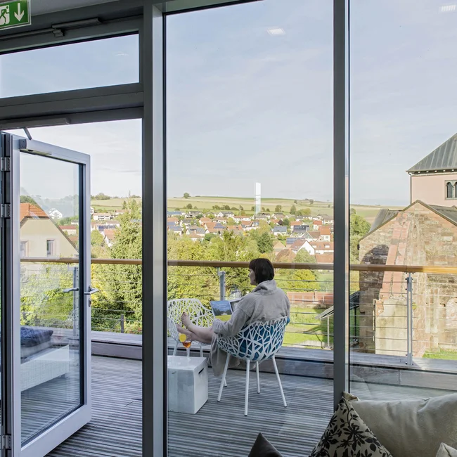 Person sitzt mit Laptop auf Balkon mit Blick auf Dorf und Kirche