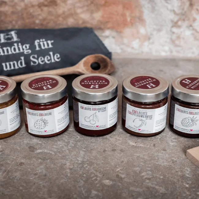 Fünf kleine Marmeladengläser mit verschiedenen Fruchtaufstrichen auf Steinboden