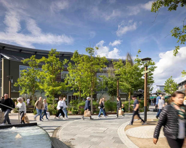 Menschen gehen im Freiluft-Einkaufszentrum an Bäumen und Brunnen vorbei