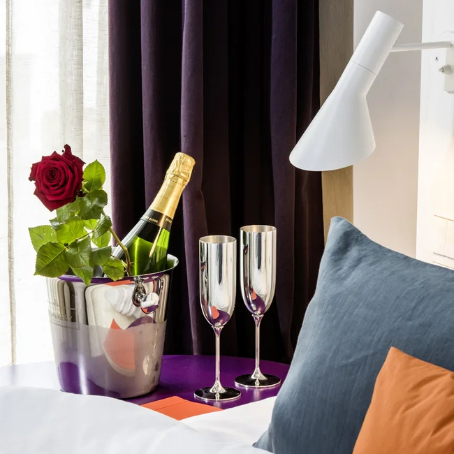 Champagnerflasche mit zwei Gläsern und roter Rose neben einem Bett