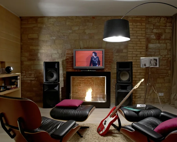 Gemütliches Wohnzimmer mit Kamin, Fernseher, Lautsprechern, Gitarren und Ledersesseln