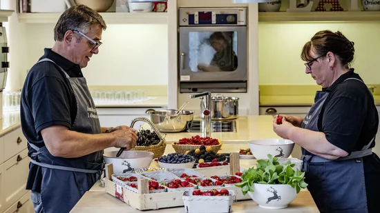 Zwei Personen bereiten frische Beeren in einer Küche mit weißen Schüsseln und Holztabletts vor