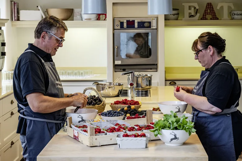Plätzchenbacken im Lösch Zwei Personen bereiten frische Beeren in einer Küche mit weißen Schüsseln und Holztabletts vor