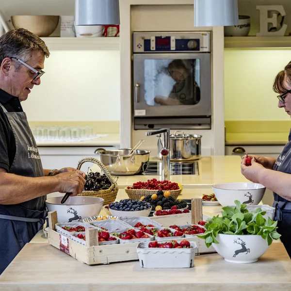 Zwei Personen bereiten frische Beeren in einer Küche mit weißen Schüsseln und Holztabletts vor