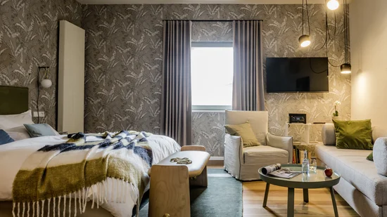 Modernes Schlafzimmer mit Bett, Sessel, Sofa, Fernseher und warmen Lampen