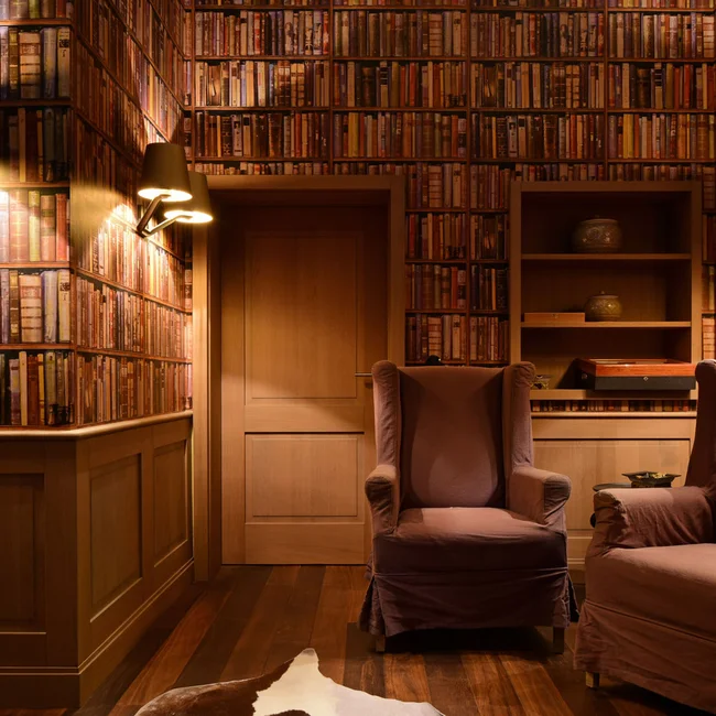 Gemütliches Zimmer mit Bücherwand, zwei Sesseln und warmem Licht