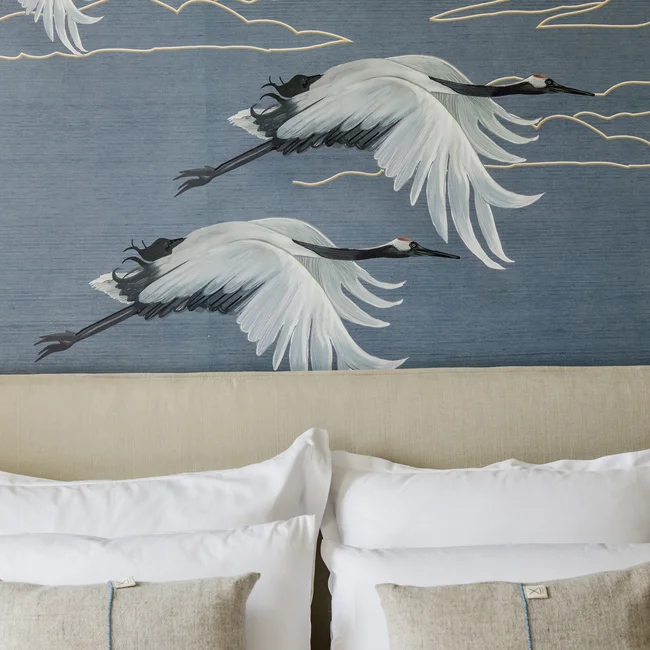 Gemälde von drei fliegenden Kranichen über einem Bett mit weißer Bettwäsche