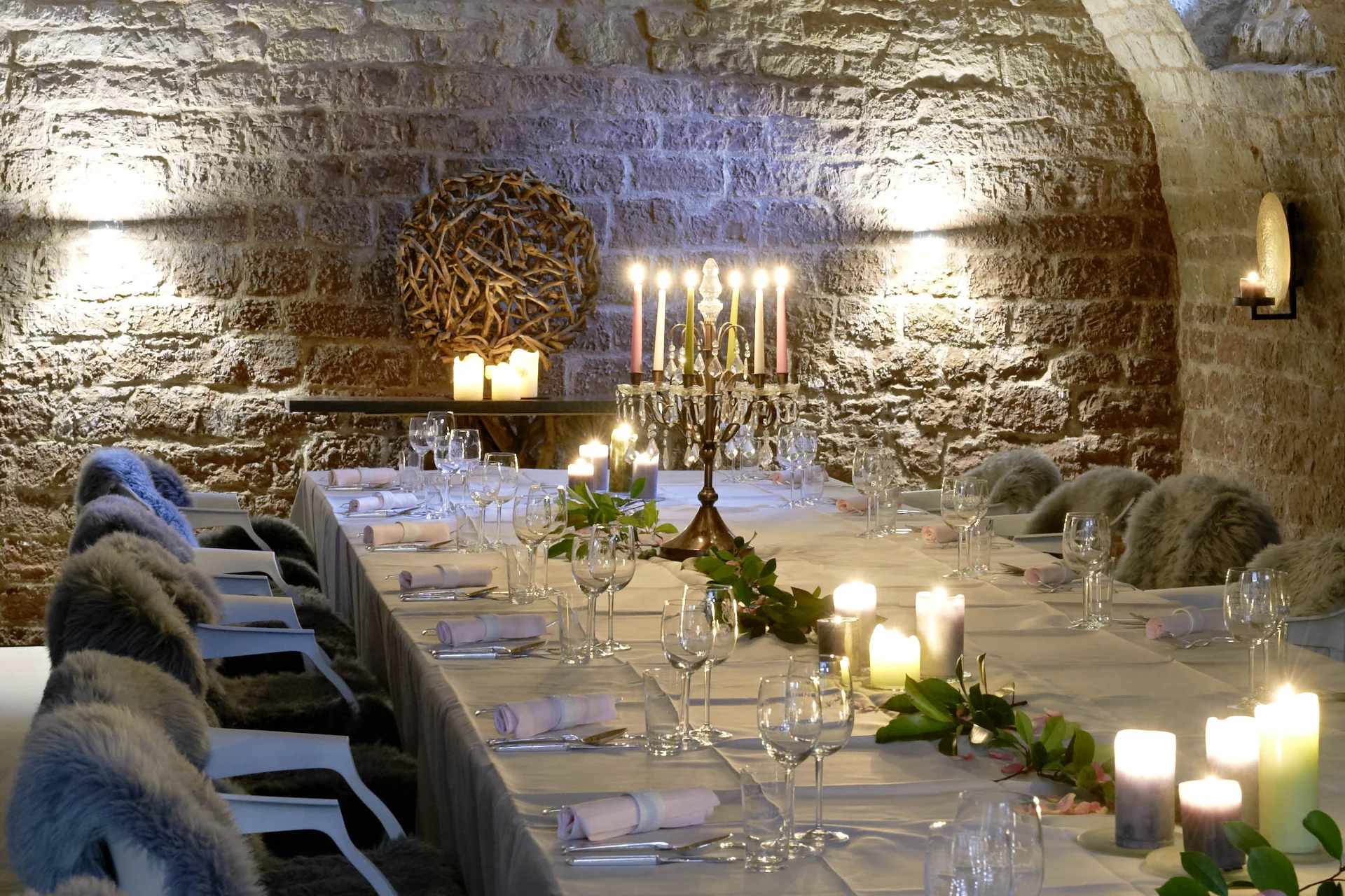 Eleganter Tisch in einem steinernen Gewölbekeller mit Kerzen und Fellen