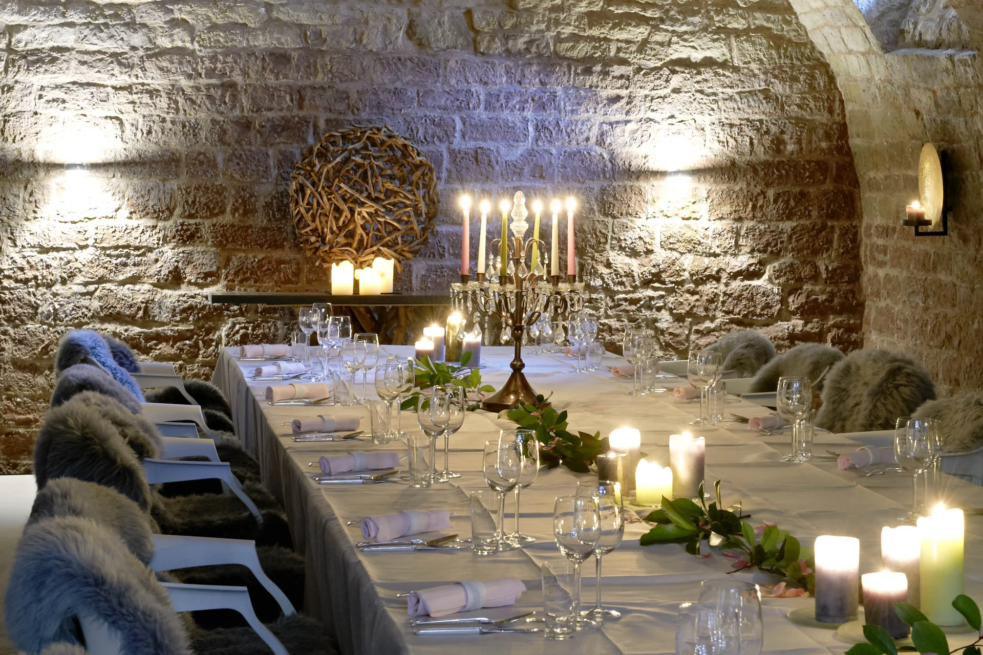 Eleganter Tisch in einem steinernen Gewölbekeller mit Kerzen und Fellen
