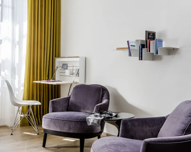 Gemütliche Sitzecke mit lilafarbenen Sesseln und Bücherregal an weißer Wand